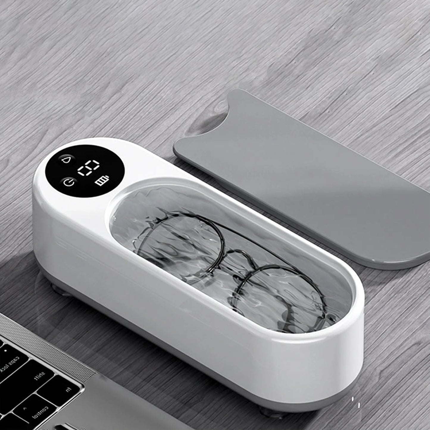 White electronic device with a digital display and glasses inside, on a wooden surface.