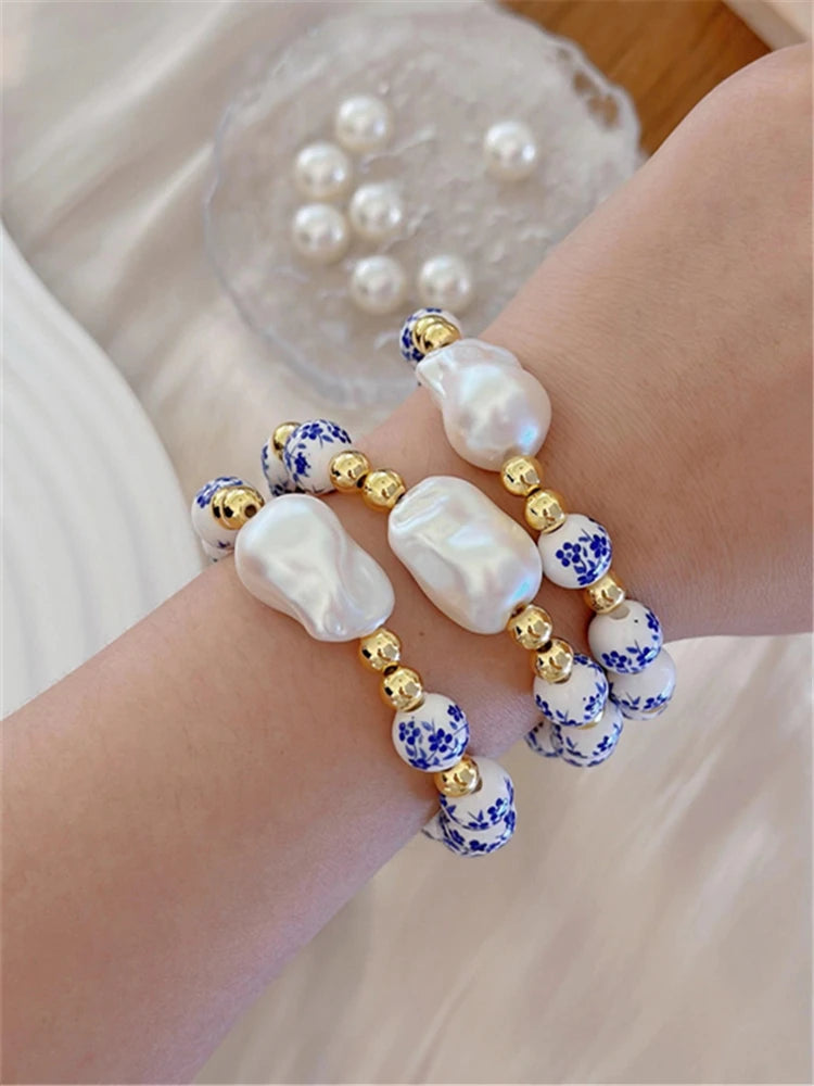 Bracelet with pearls and blue floral beads on a wrist, with a glass container of additional pearls in the background.