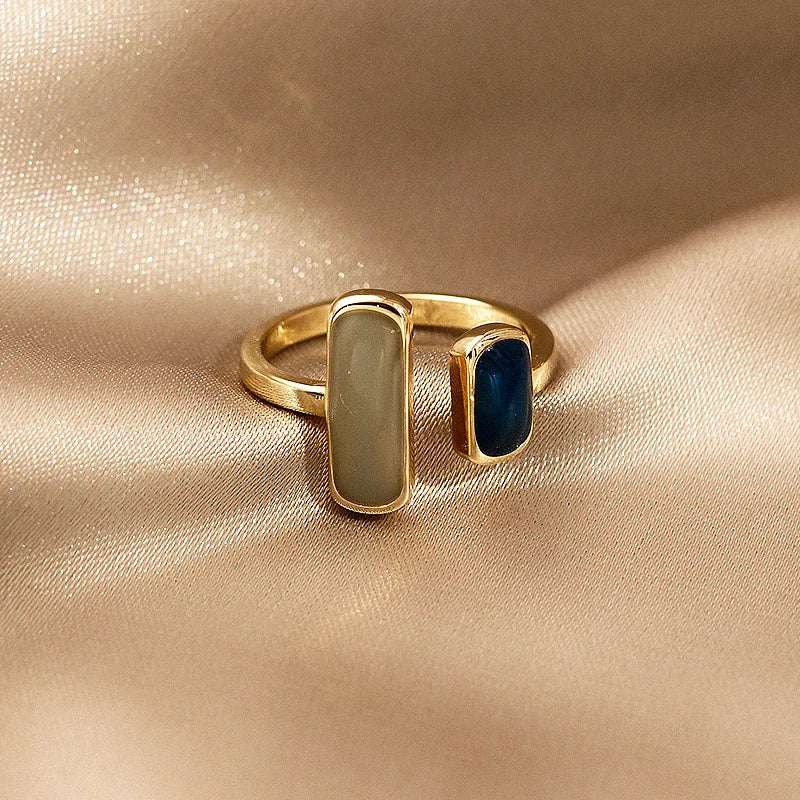 Gold ring with two colored stones on a beige fabric background