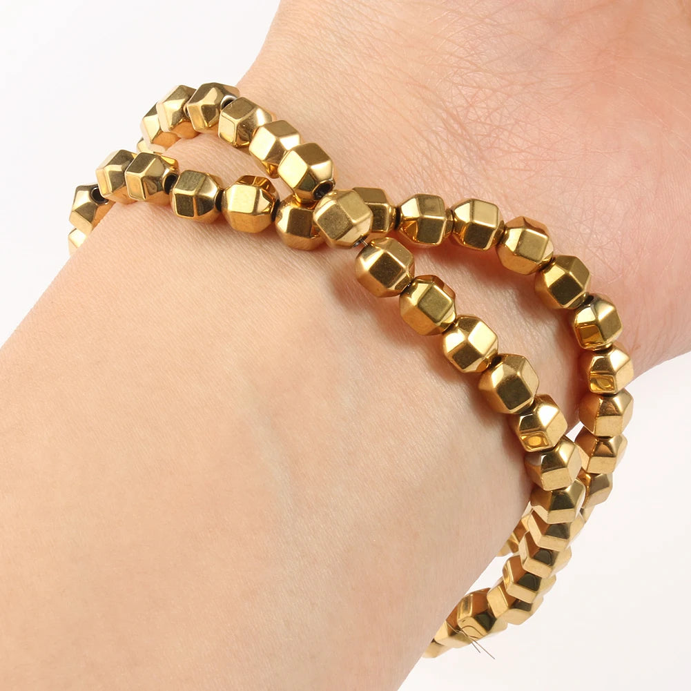 Gold beaded bracelet on a wrist against a neutral background