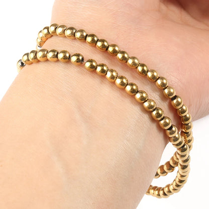 Gold beaded bracelet on a wrist against a neutral background