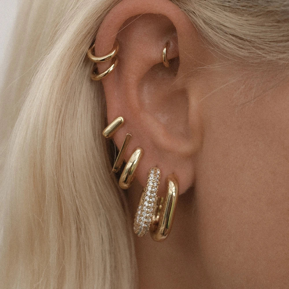 Close-up of an ear wearing multiple gold hoop earrings with a blurred background.