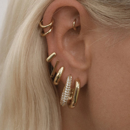 Close-up of an ear wearing multiple gold hoop earrings with a blurred background.