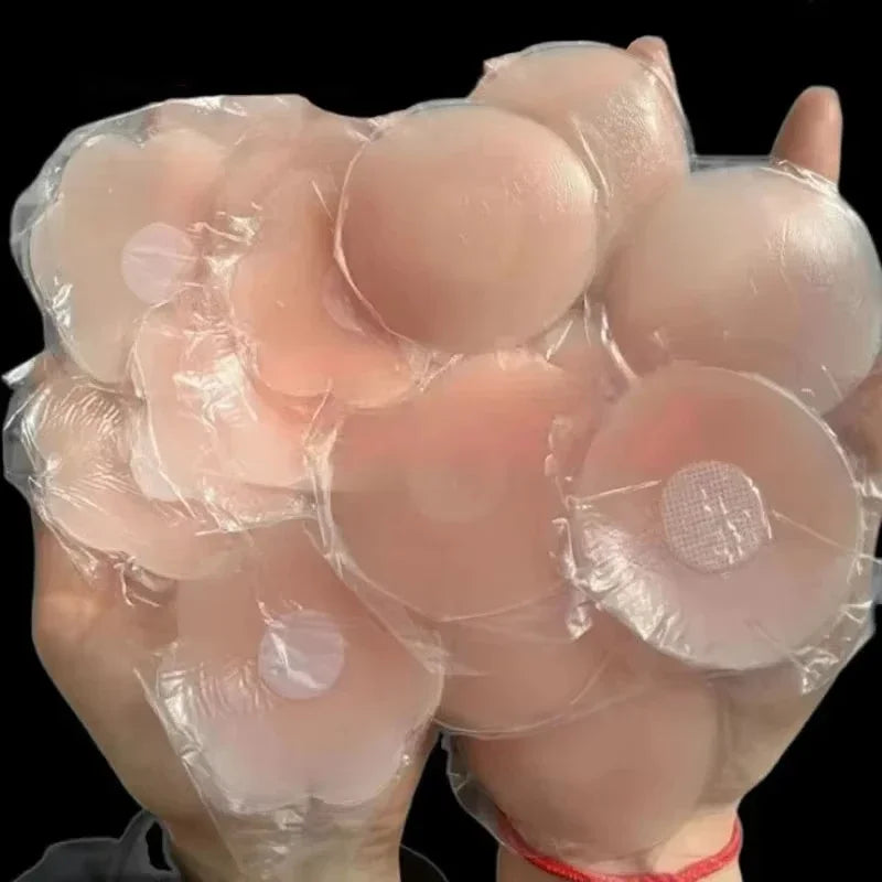 Multiple silicone breast forms wrapped in clear plastic held by a gloved hand against a black background.