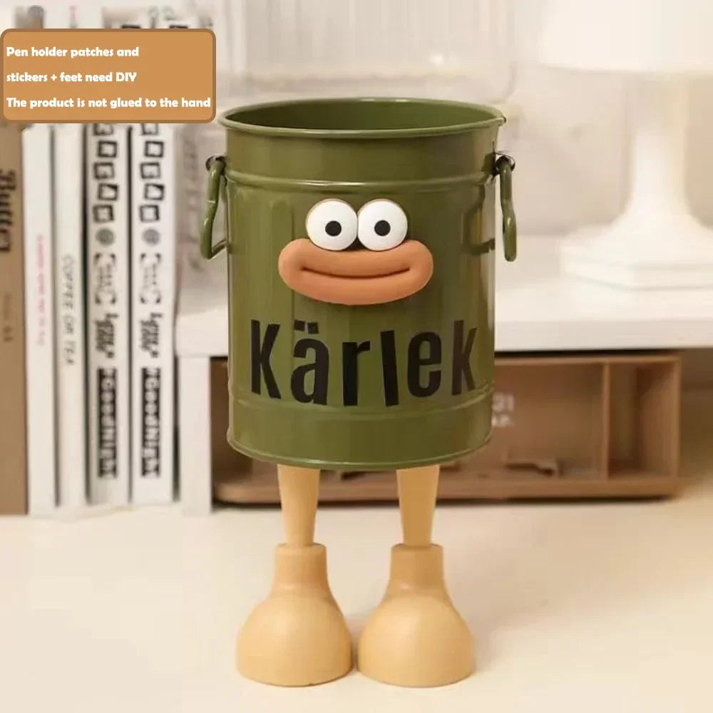 Green bucket with a face and 'Kärlek' text, standing on a surface with books in the background.