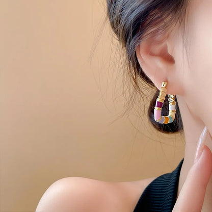 Close-up of a person wearing colorful hoop earrings against a beige background