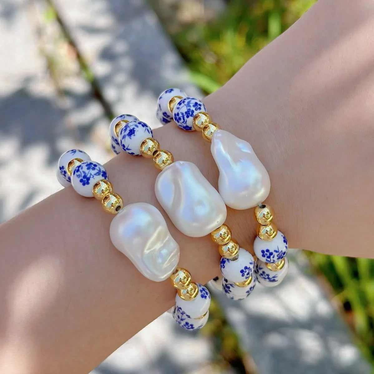 Beaded bracelet with pearls and blue floral patterns on a wrist against a blurred natural background