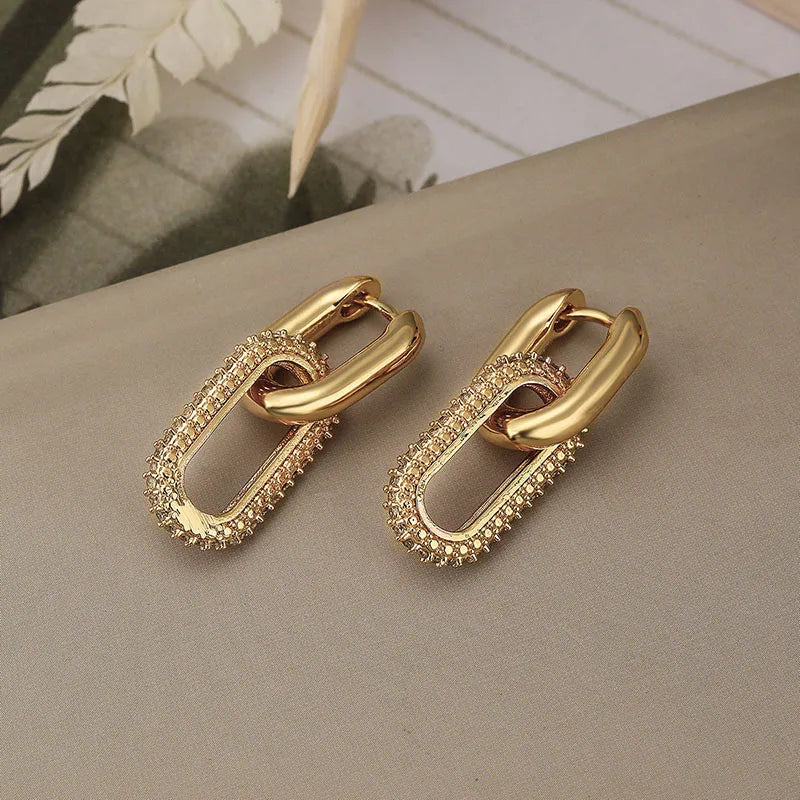 Gold chain-style earrings on a neutral surface with a blurred background