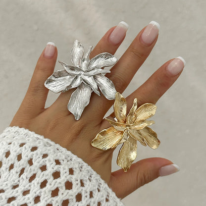Silver and gold flower-shaped rings on a hand with a neutral background