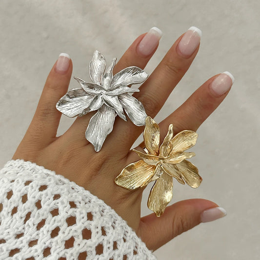 Silver and gold flower-shaped rings on a hand with a neutral background