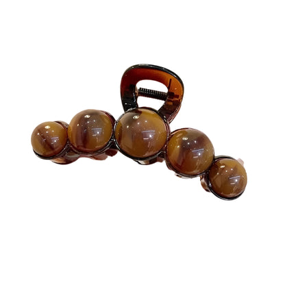 Hand holding a hair clip with brown beads against a neutral background