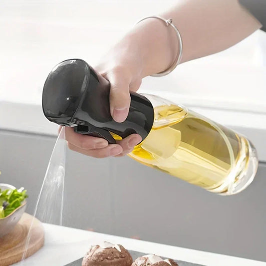 Person using a handheld sprayer to mist a bottle of olive oil over food on a kitchen counter.