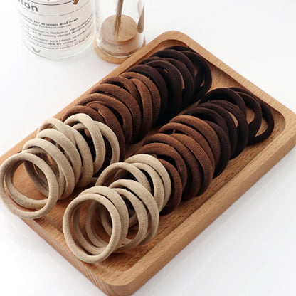 Set of brown and beige hair ties on a wooden tray with a white background