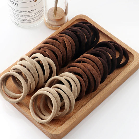 Set of brown and beige hair ties on a wooden tray with a white background