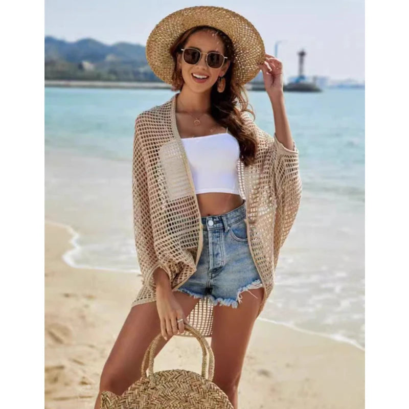 Woman on a beach wearing a straw hat, white top, denim shorts, and a beige mesh cover-up.