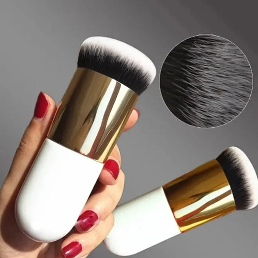 Makeup brush with gold and white handle held by a hand with red nail polish, close-up of bristles on gray background.