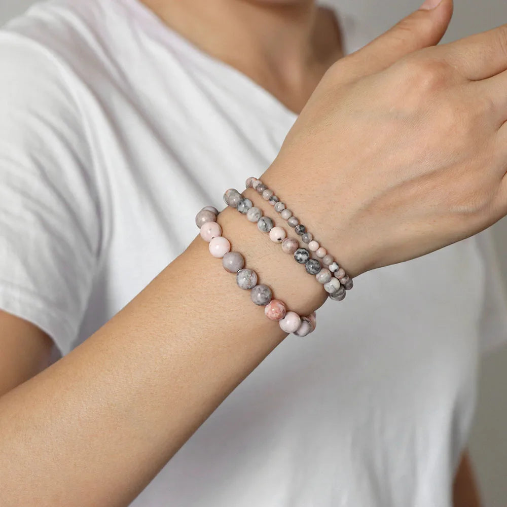 Person wearing two beaded bracelets on a plain background