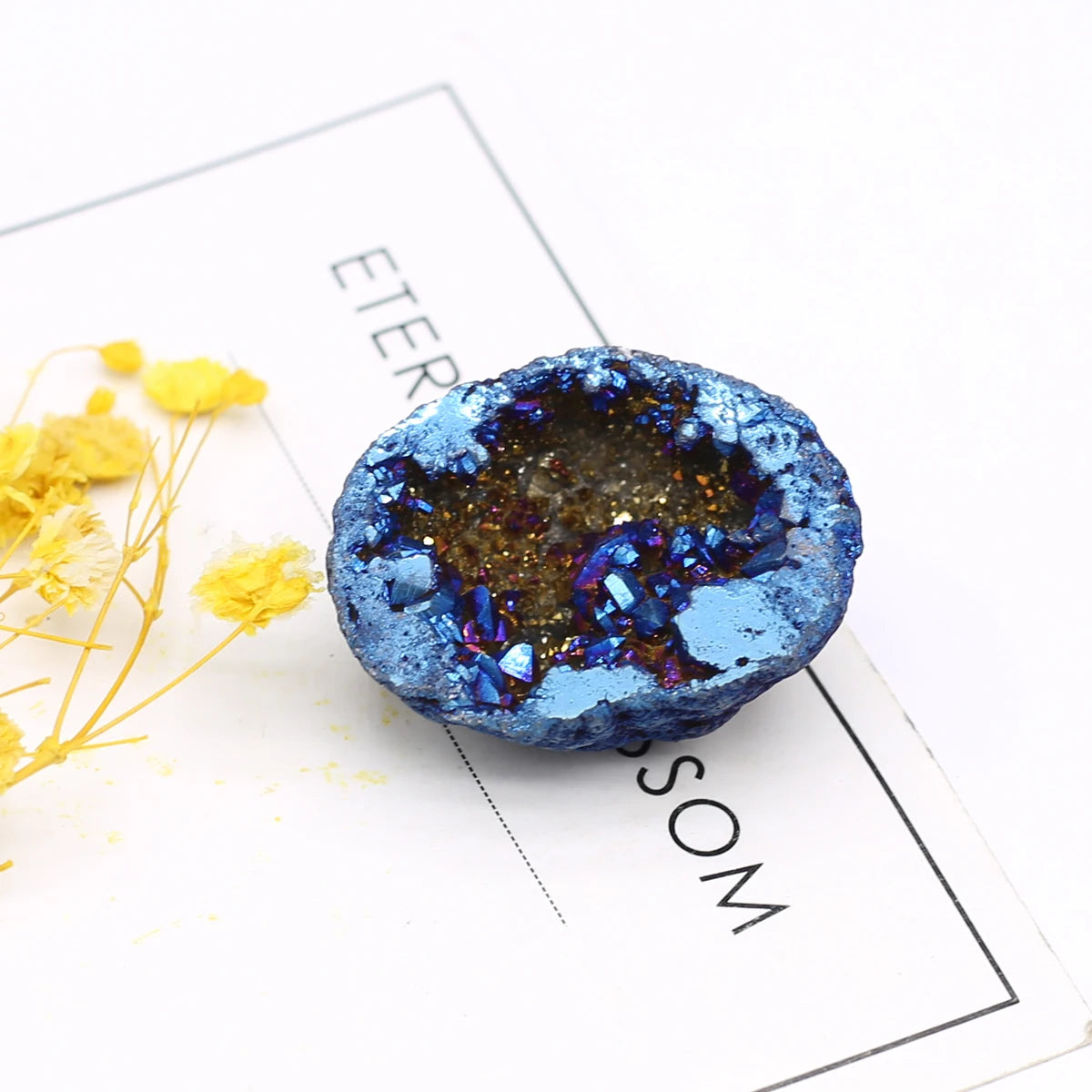 Blue geode crystal on a white surface with yellow flowers