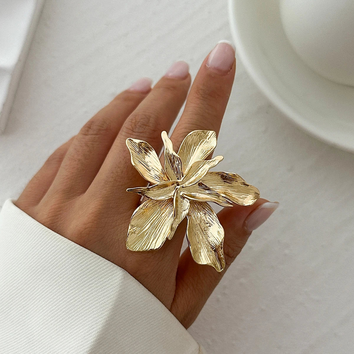 Gold floral ring on a hand with a light background