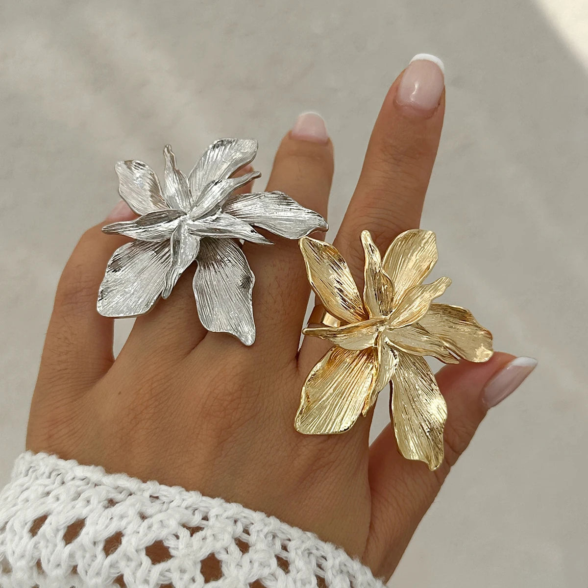 Gold and silver floral rings on a hand with a neutral background