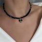 Black beaded necklace with a heart-shaped pendant on a person wearing a white top.