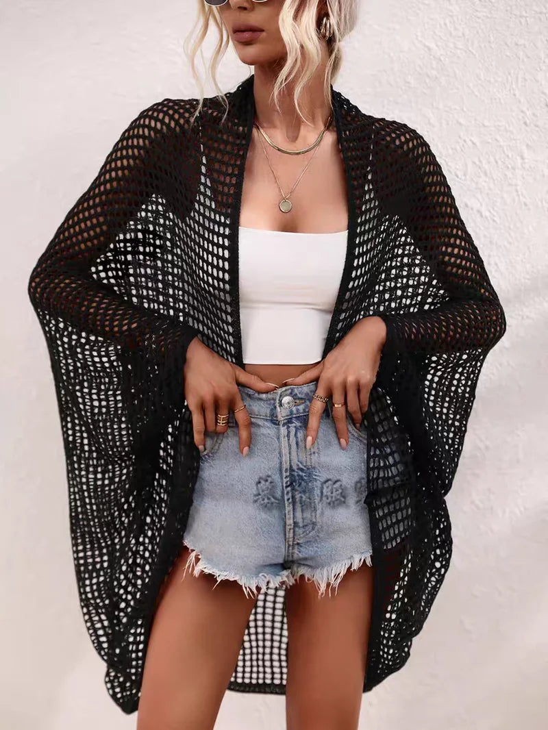 Woman wearing a black mesh cover-up over a white top and denim shorts on a plain background