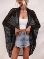 Woman wearing a black mesh cover-up over a white top and denim shorts on a plain background