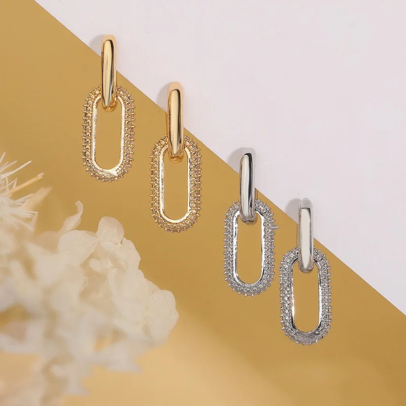 Gold and silver chain-style earrings on a yellow and white background