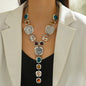 Necklace with multicolored stones worn by a person in a white blazer.