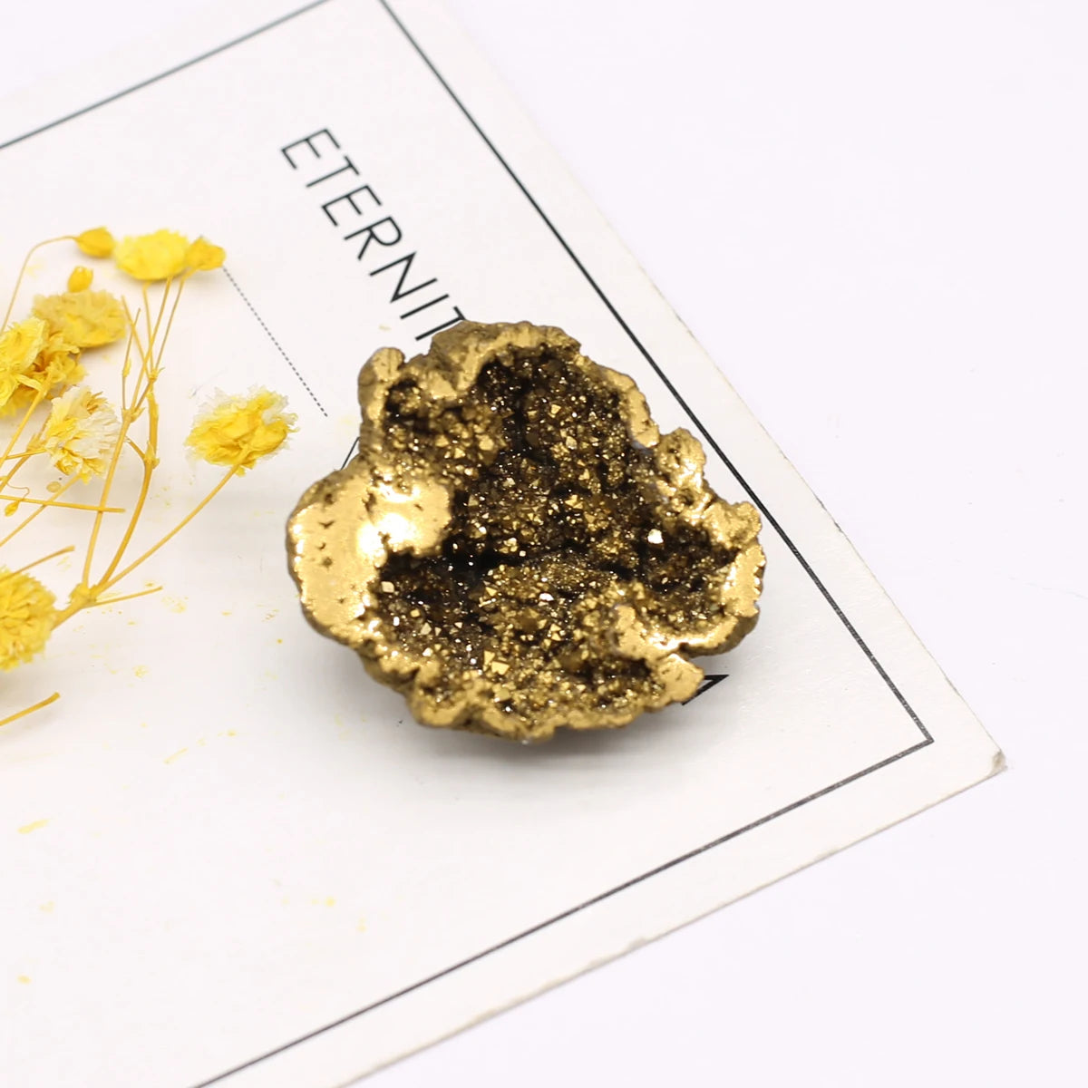 Gold decorative rock on a white surface with yellow flowers