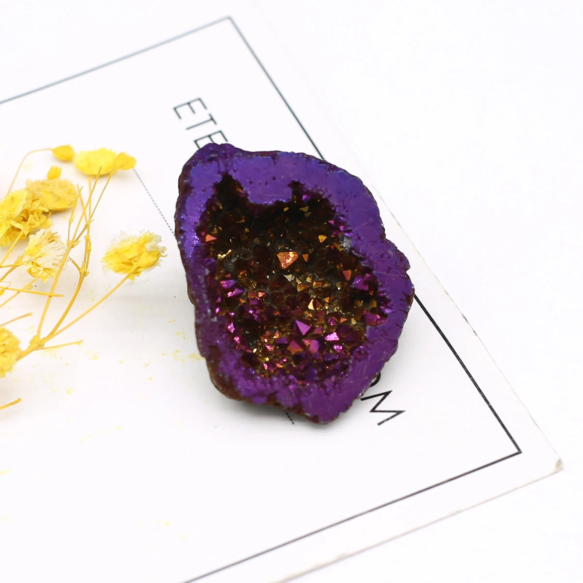 Purple geode crystal on a white surface with yellow flowers