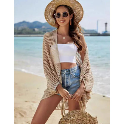 Woman on a beach wearing a straw hat, sunglasses, and a white top with denim shorts.