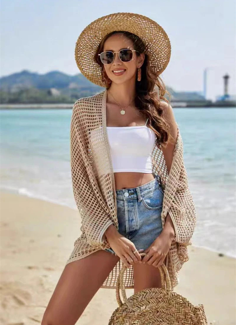 Woman on a beach wearing a straw hat, white top, denim shorts, and a beige cardigan.
