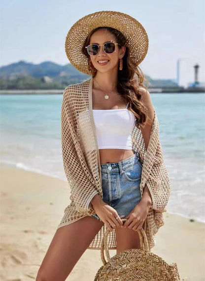 Woman on a beach wearing a straw hat, white top, denim shorts, and a beige cardigan.