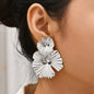 Silver floral earrings worn by a person with a blurred background