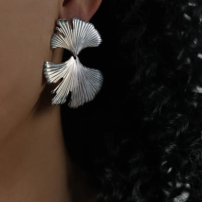 Silver leaf-shaped earring worn on an ear with a dark background