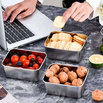 Metal snack containers with food on a desk next to a laptop