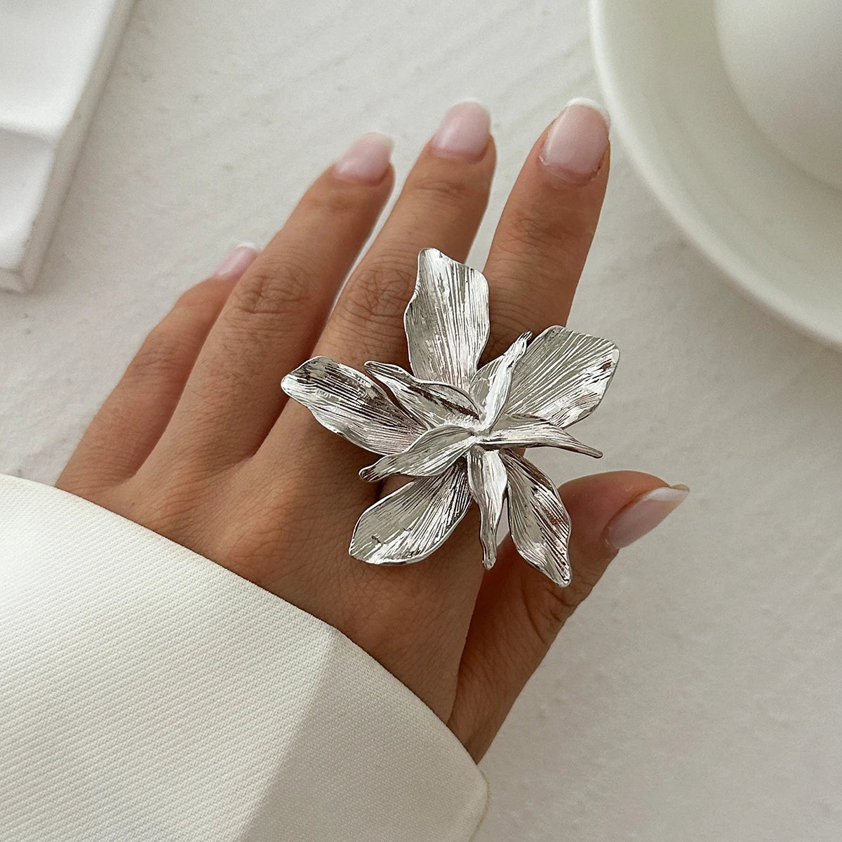 Silver floral ring on a hand with a neutral background