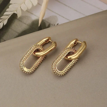 Gold chain-style earrings on a neutral surface with a blurred background