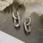 Pair of silver hoop earrings on a reflective surface with a soft background