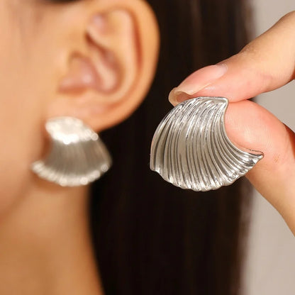 Silver shell-shaped earrings being held up to a person's ear.