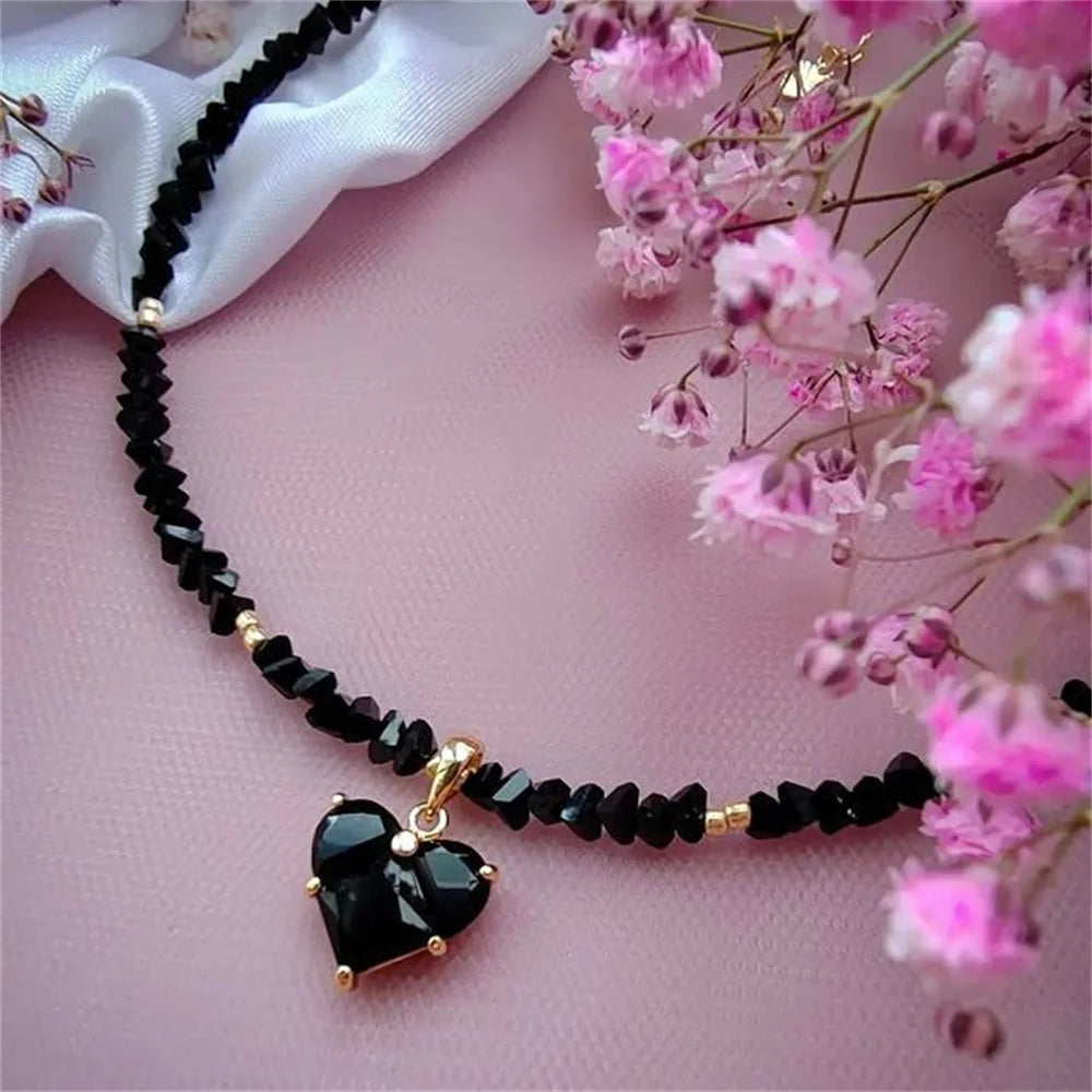Necklace with black beads and a heart-shaped pendant on a pink background with pink flowers.