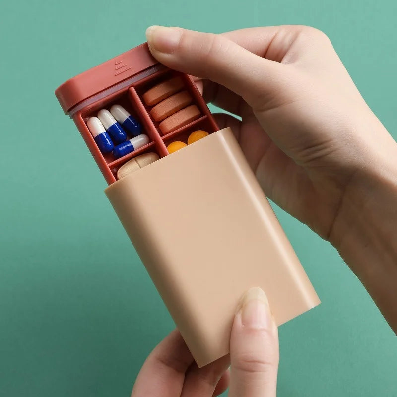 Hand holding a pill organizer with various colored pills against a green background