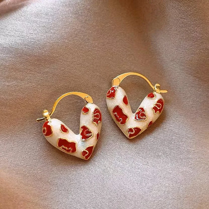 Heart-shaped earrings with red and gold design on a beige background