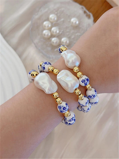 Bracelet with pearls and blue floral beads on a wrist, with a glass container of additional pearls in the background.