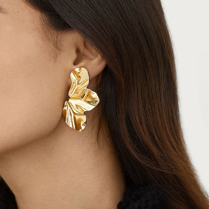 Gold leaf-shaped earring worn by a person with a neutral background