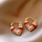 Pair of earrings with pink, red, and gold design on a beige fabric background
