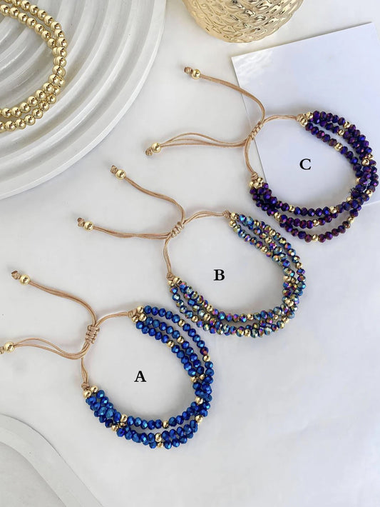 Three beaded bracelets on a white surface with gold accents