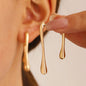 Gold earrings being worn with a neutral background