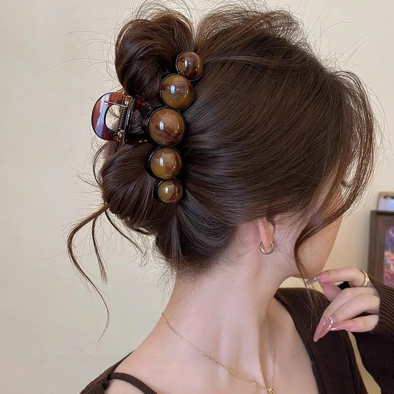 Woman with a stylish hair bun using wooden hair accessories against a neutral background